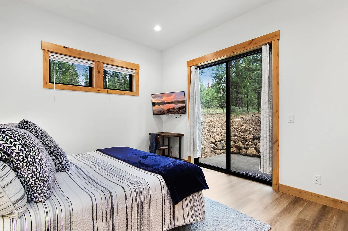 Bedroom featuring a bed with patterned pillows, wood-trimmed windows, a wall-mounted TV, and sliding glass doors leading to a patio.