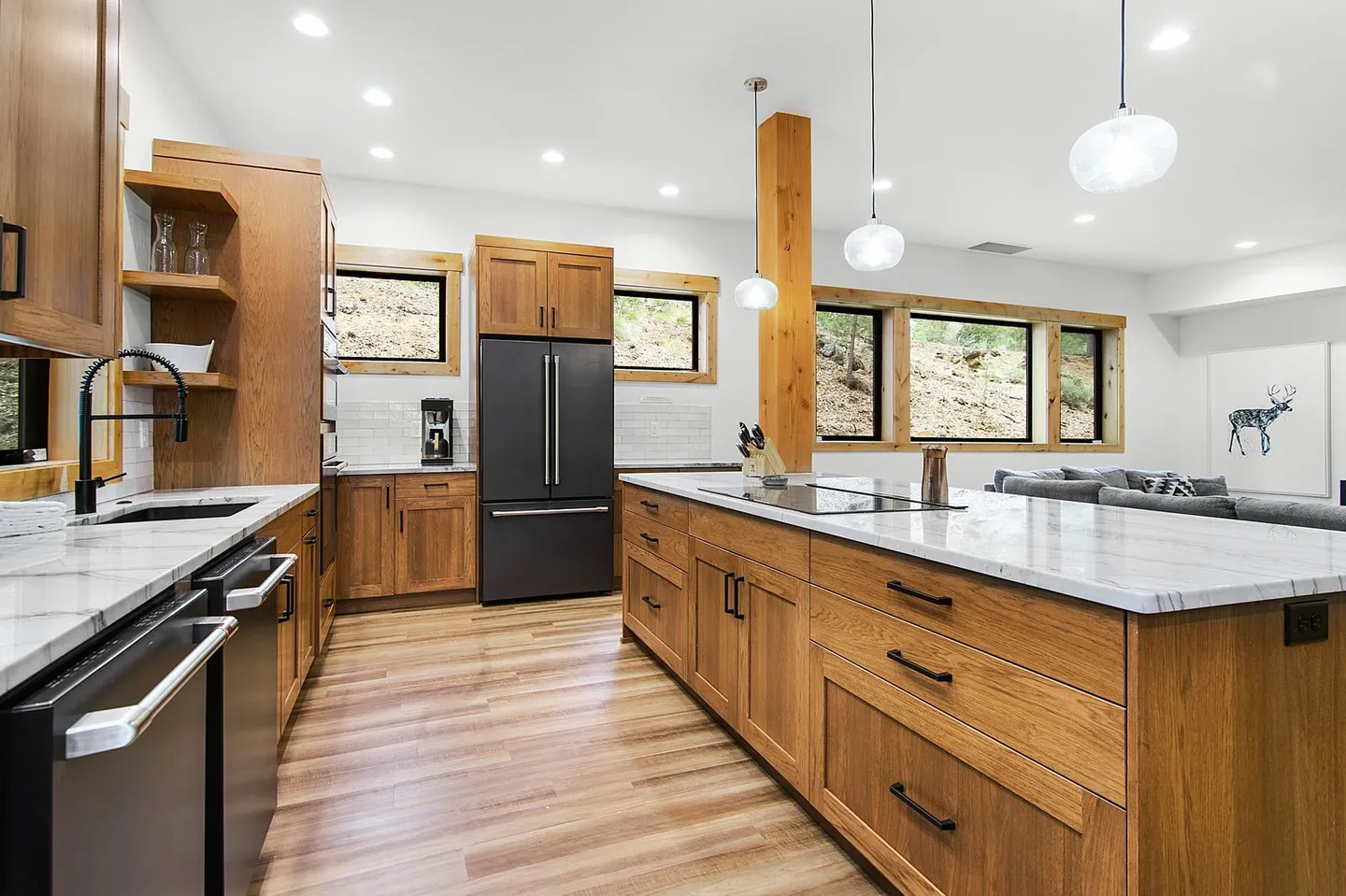 Open-concept modern kitchen featuring light wood cabinetry, light marble-style countertops, dark appliances, a large center island, and wood floors.