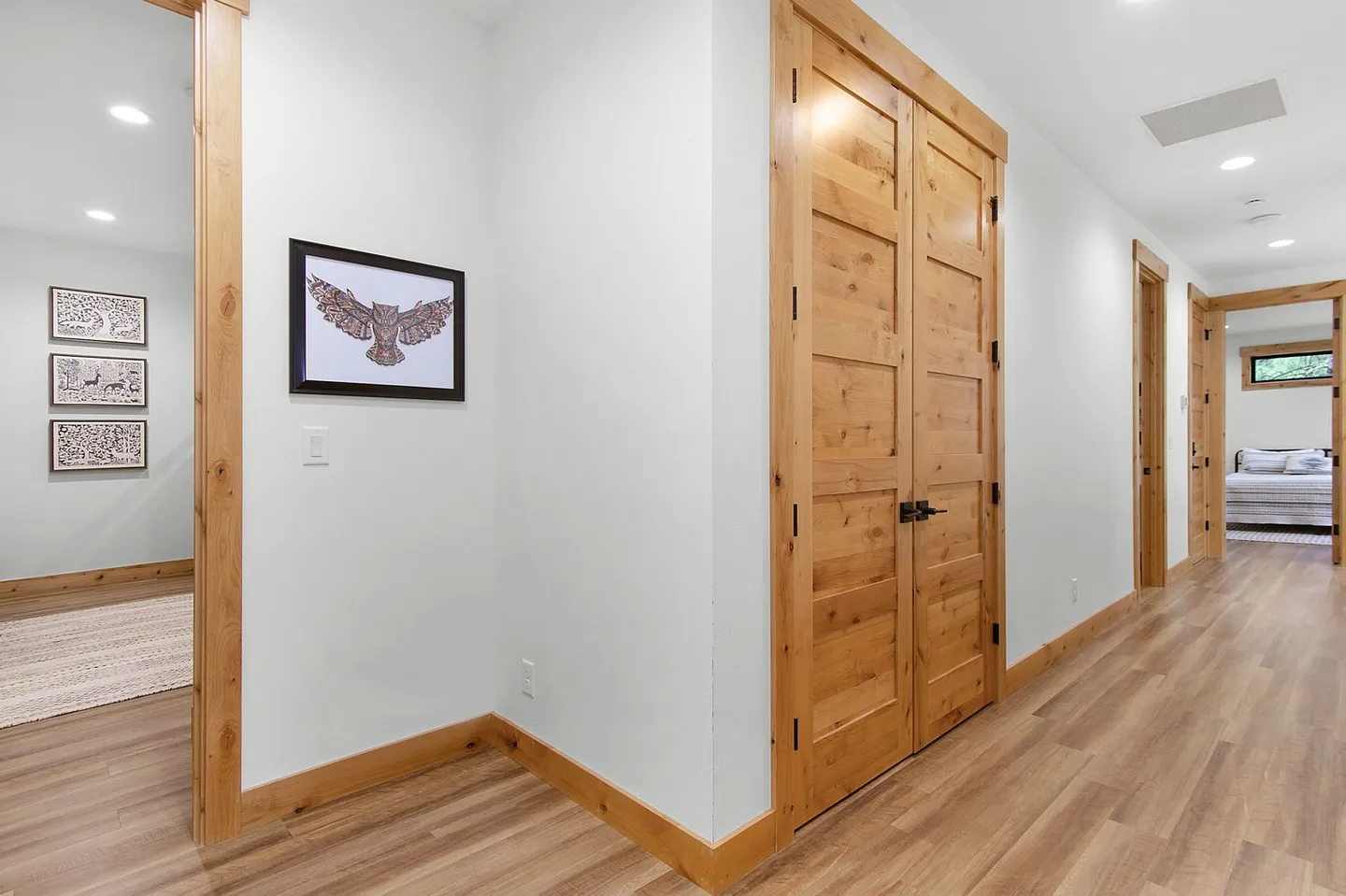 Hallway featuring light wood-look flooring, light-colored walls, and natural wood double doors and trim.