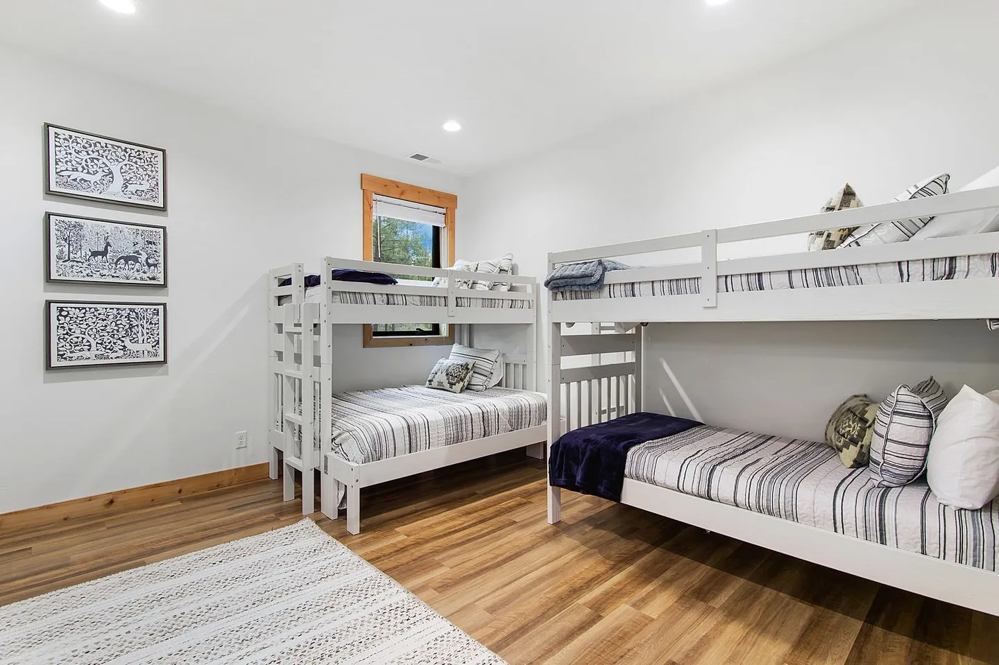 Bedroom with two sets of white wooden bunk beds and wood-look flooring.