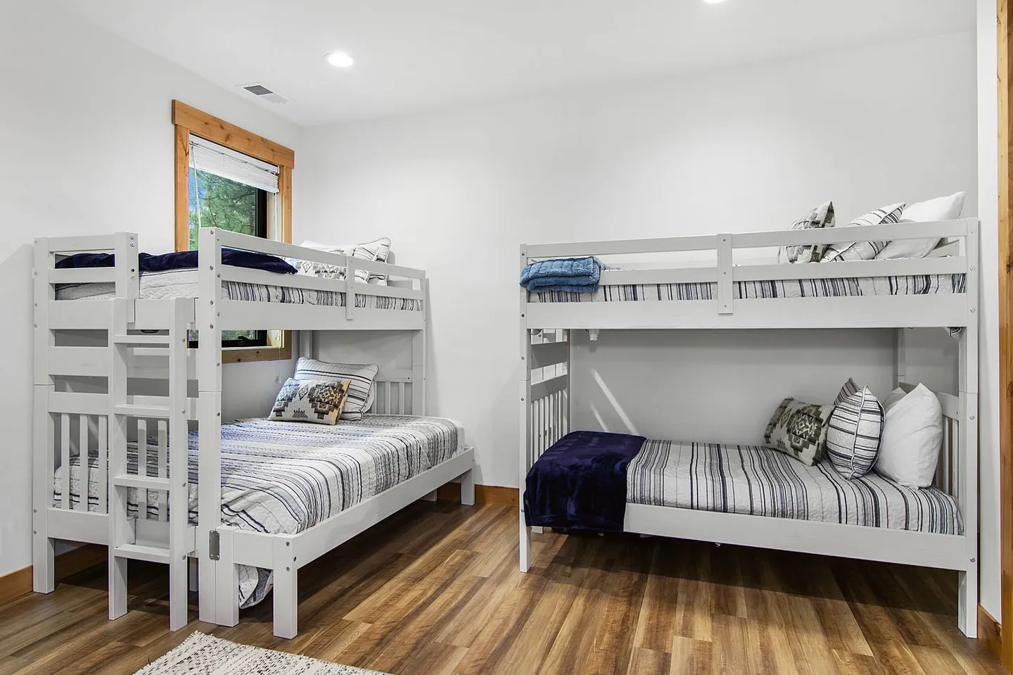 Bedroom featuring two sets of white painted wooden bunk beds on wood-look flooring.