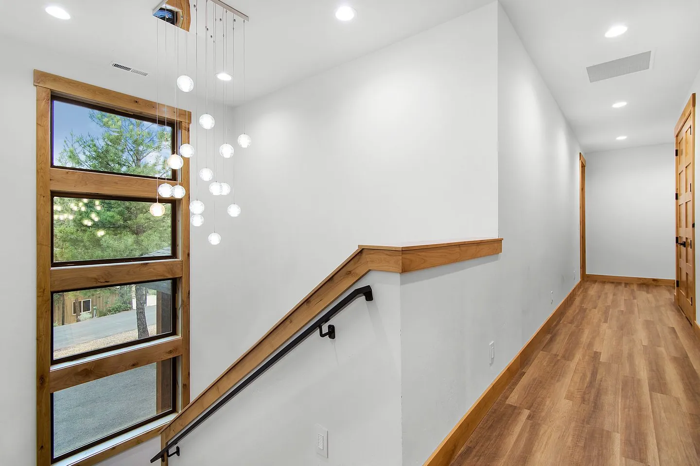 Stairwell landing and hallway featuring light wood flooring, white walls, stacked rectangular windows, and a multi-pendant orb light fixture.
