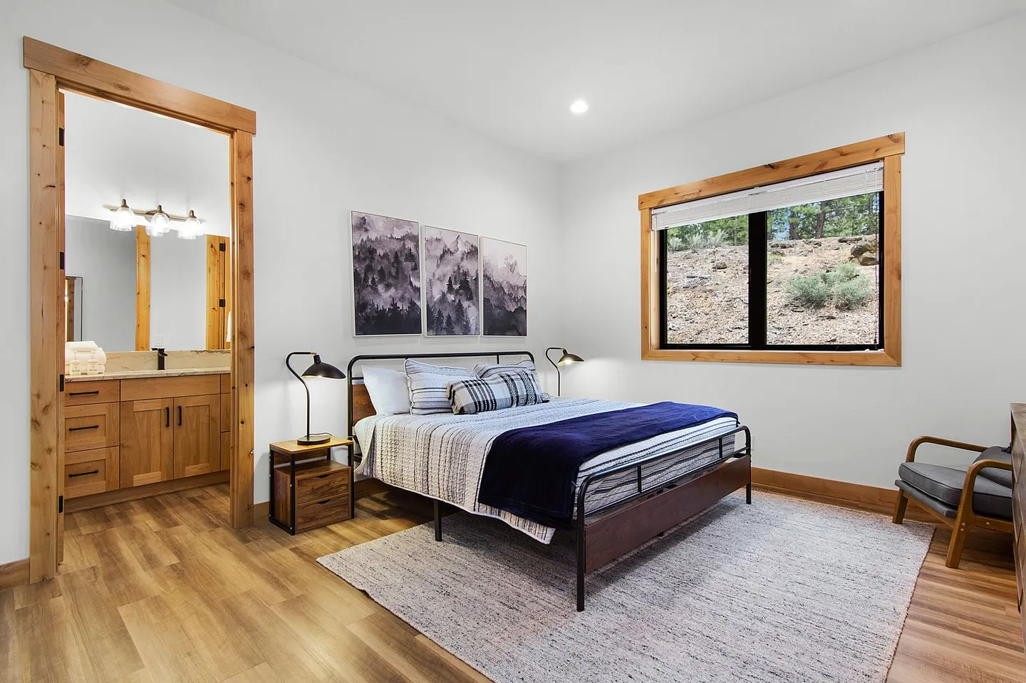 Bedroom with a metal-frame bed, bedside tables with lamps, a window looking outside, and an open doorway to an ensuite bathroom.