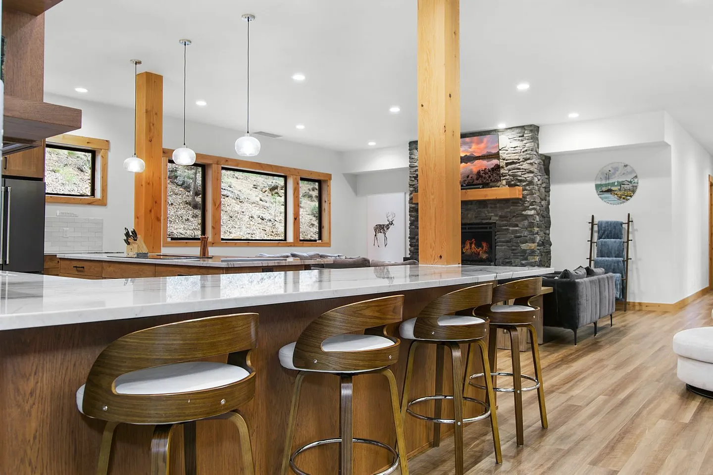 Kitchen island with barstools looking into an open-concept living area with a stone fireplace.