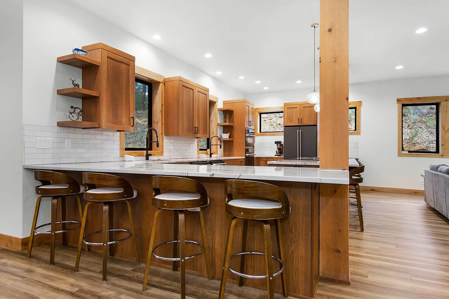 Kitchen island with four modern wooden barstools with white cushions, wood cabinetry, and stainless steel appliances.