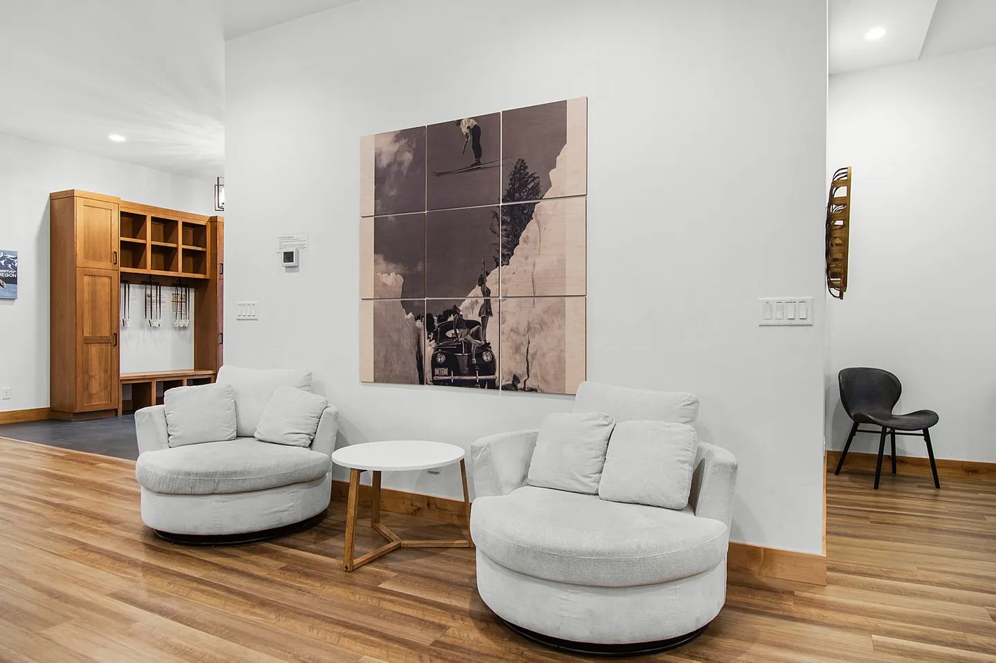 Seating area with two rounded armchairs, a small round table, and wood-look flooring, with a mudroom area visible in the background.