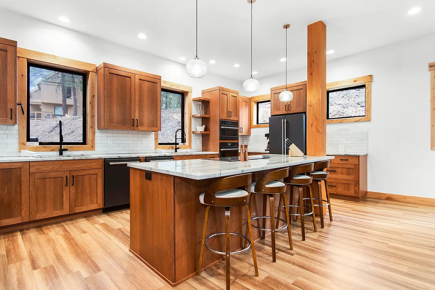 Modern kitchen with wood cabinetry, marble-style island, black appliances, and pendant lighting over barstools.
