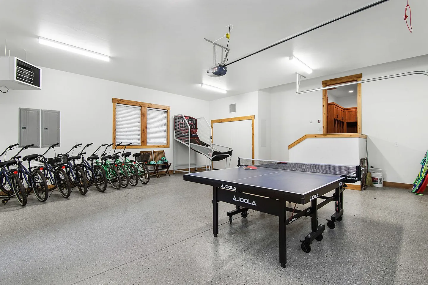 Garage converted into a game room with a ping-pong table, arcade basketball game, and several parked bicycles.