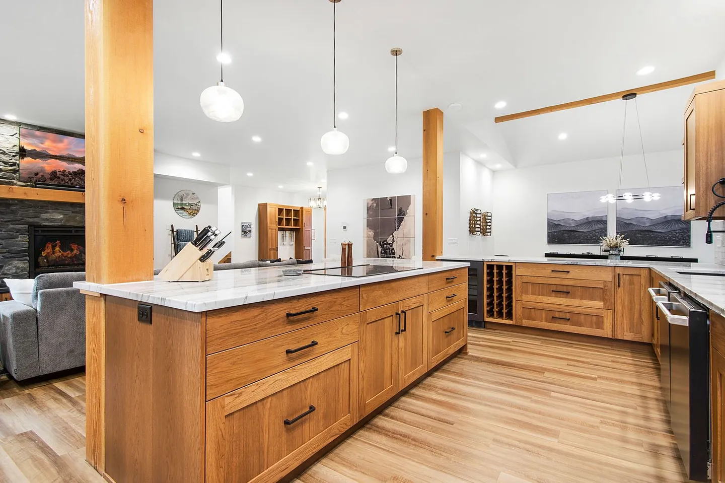 Open-concept modern kitchen featuring a wood island with light marble countertops, pendant lights, and a view into the living room with a fireplace.