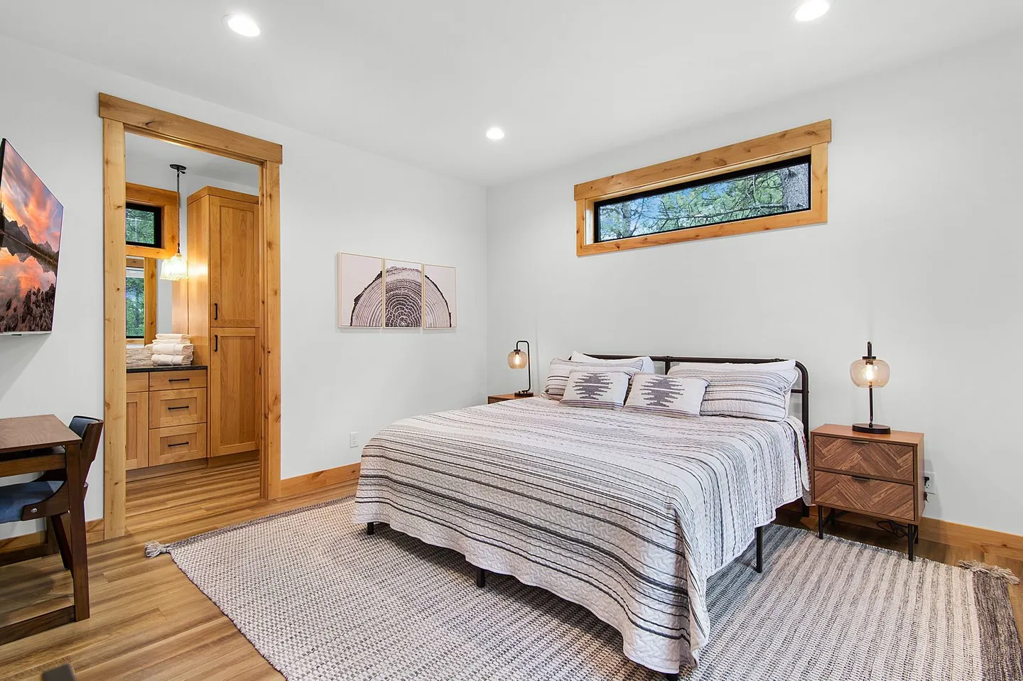 Bedroom with a patterned bedspread, area rug, wooden nightstands, narrow high window, and doorway to an ensuite bathroom.