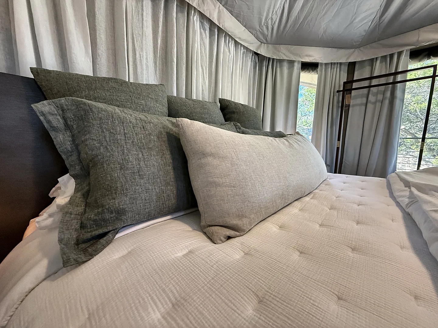 Close-up of a bed with white textured bedding and gray pillows against draped fabric walls.