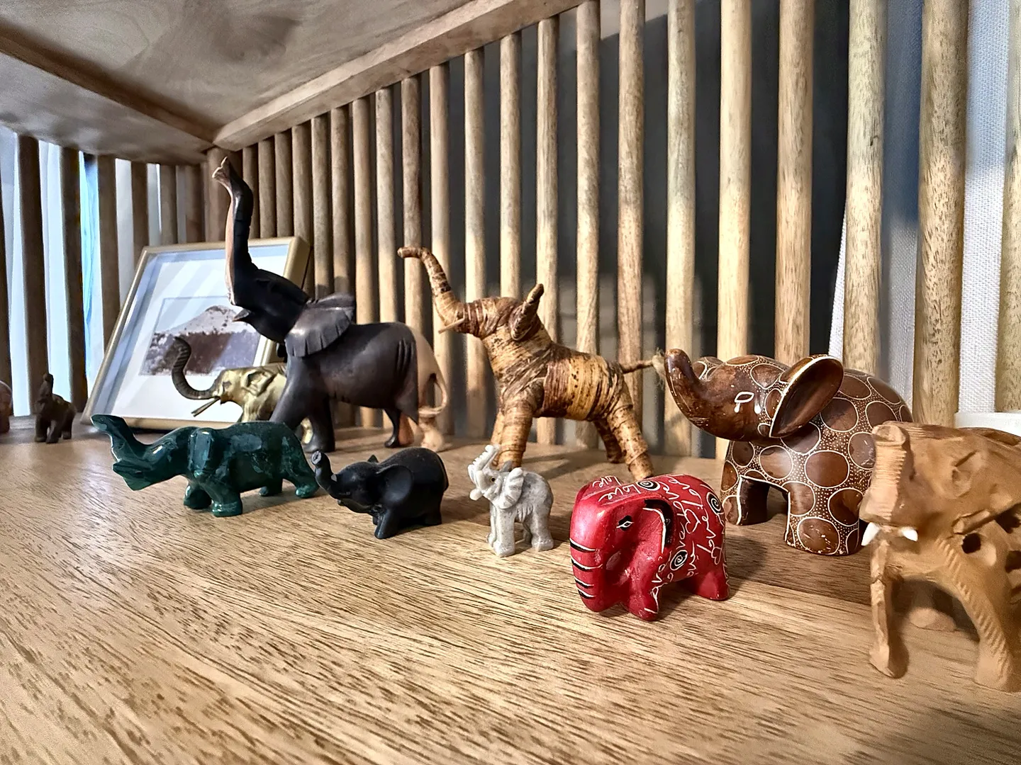 Close-up of a collection of small elephant figurines made of various materials displayed on a wooden shelf.