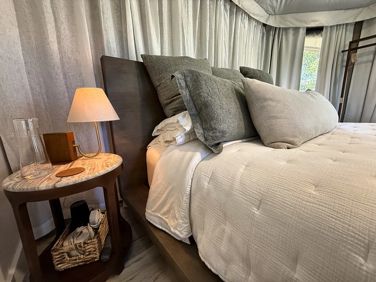 Close-up view of a made bed with textured pillows and a wooden nightstand with an illuminated small lamp.