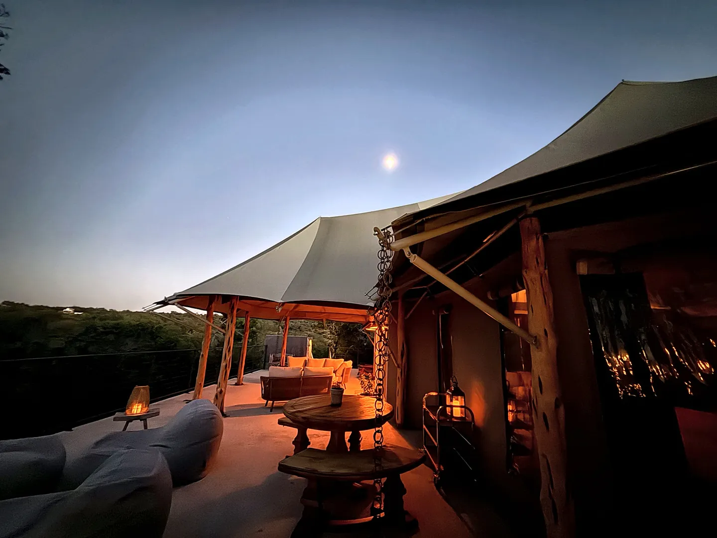 Outdoor deck under canvas canopy tents illuminated at dusk with warm lantern lighting and seating areas.
