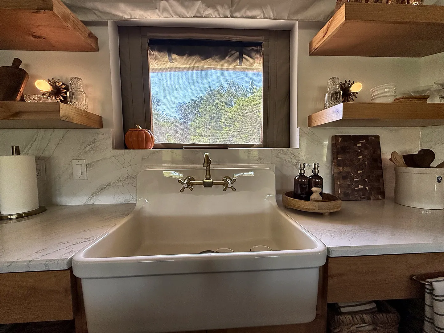 A farmhouse sink with brass fixtures centered beneath a small window flanked by open wood shelving.