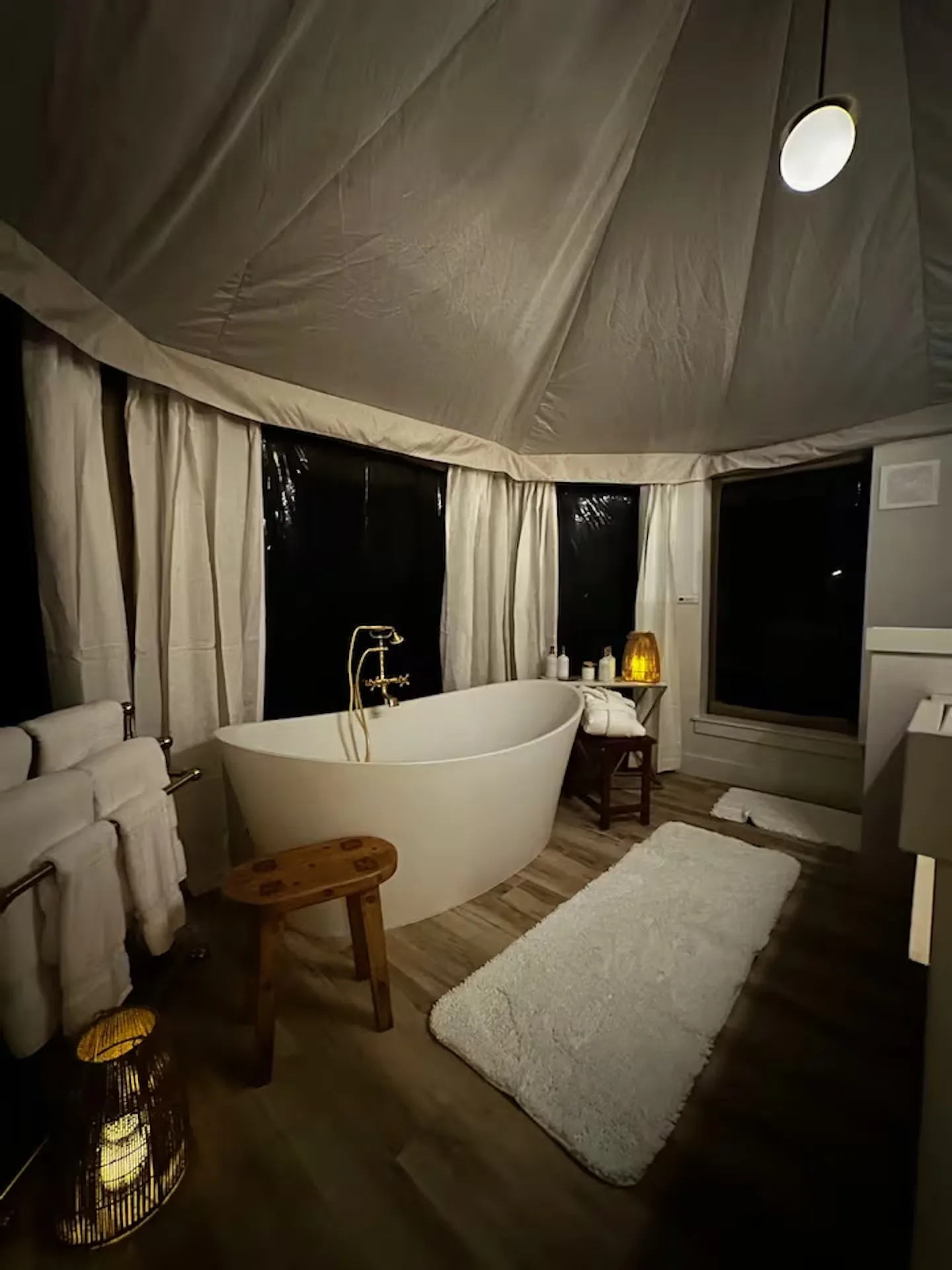 Freestanding soaking tub inside a tent-style bathroom with soft ambient lighting at night.