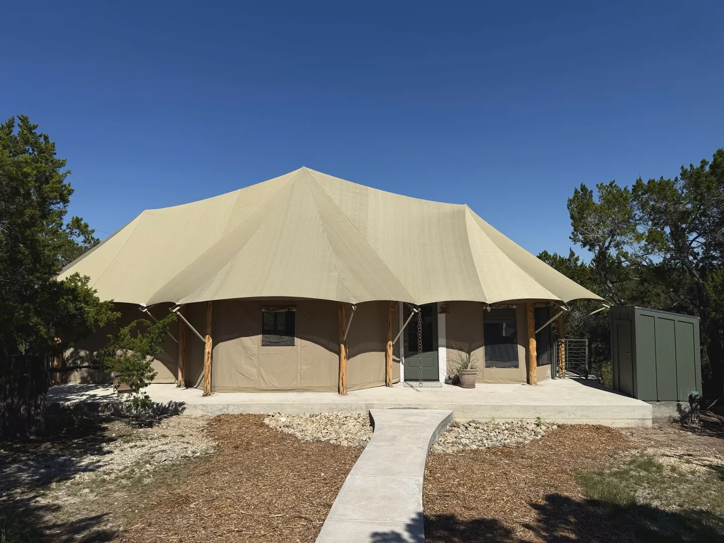 Exterior view of a large safari-style glamping tent on a concrete foundation under a clear blue sky.