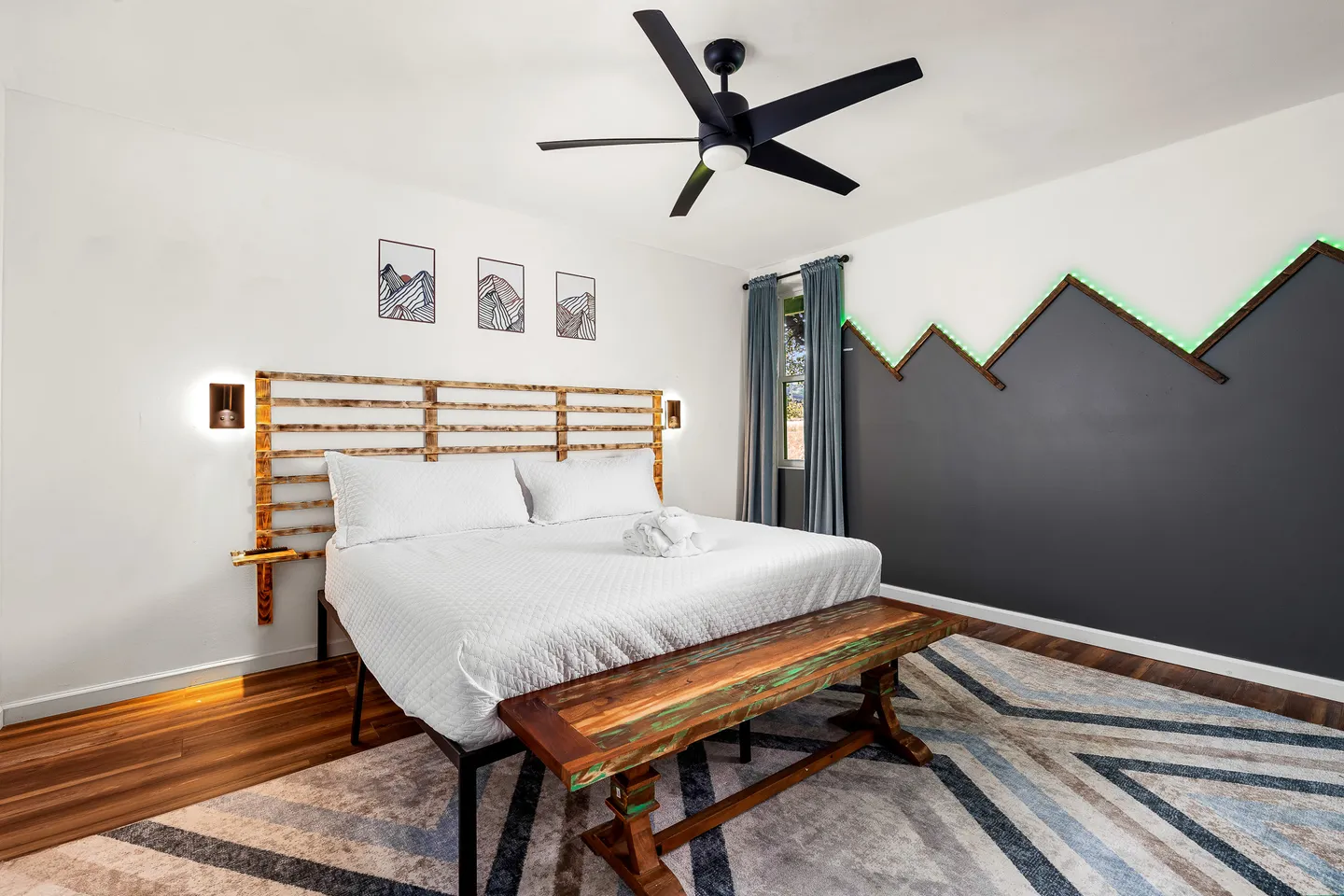 Bedroom with a bed featuring a slatted wooden headboard, a wooden bench, and a geometric mountain accent wall with green backlighting.