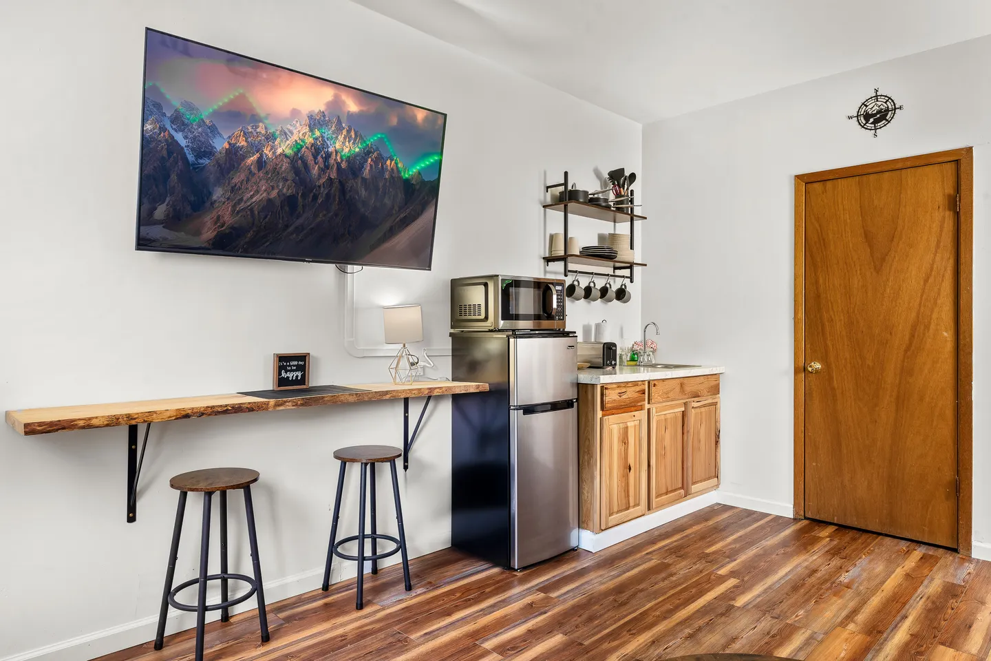 Kitchenette and bar seating area with a mini fridge, microwave, wall-mounted television, and wood laminate floors.