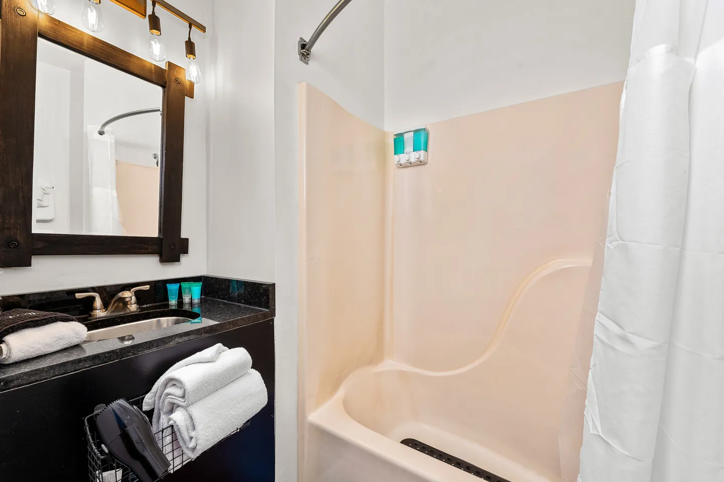 Bathroom with a dark vanity topped by a wood-framed mirror next to a beige shower and bathtub combination.