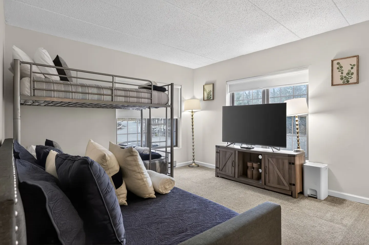 Bedroom featuring a metal bunk bed, a sofa bed in the foreground, carpeted flooring, and a flat-screen TV on a wooden console.