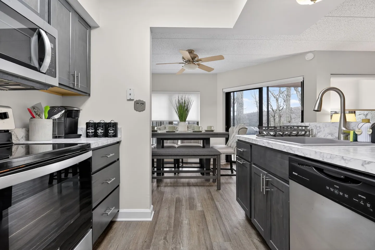 Kitchen with dark grey cabinets and marble-look counters looking into an adjacent dining area.