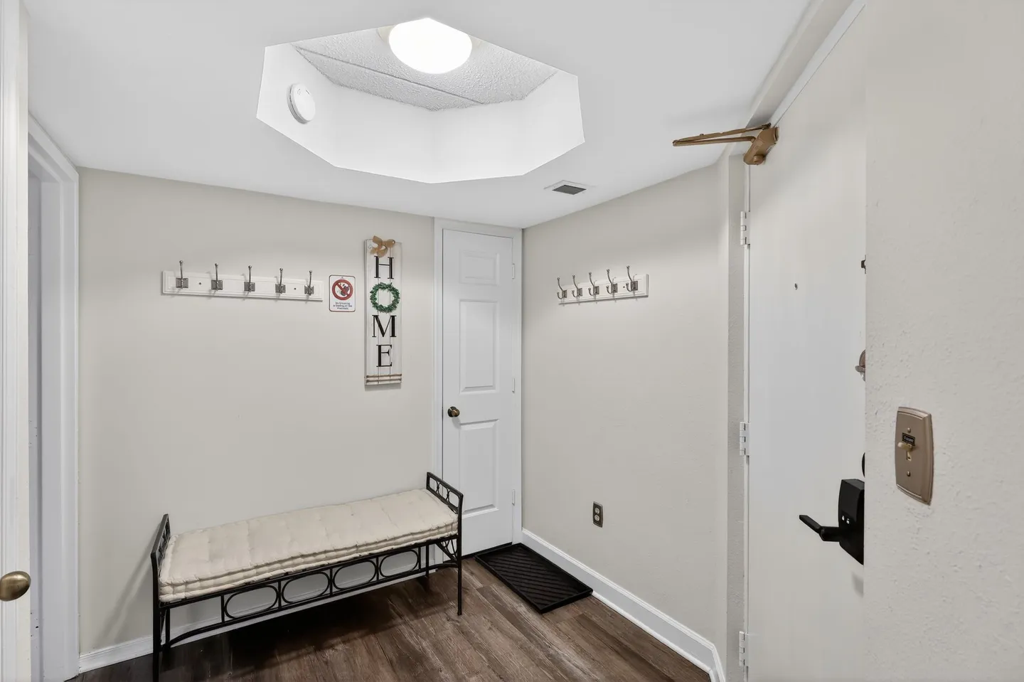 Entryway with a cushioned metal bench, coat hooks on the walls, wood-style flooring, and an octagonal recessed ceiling light.