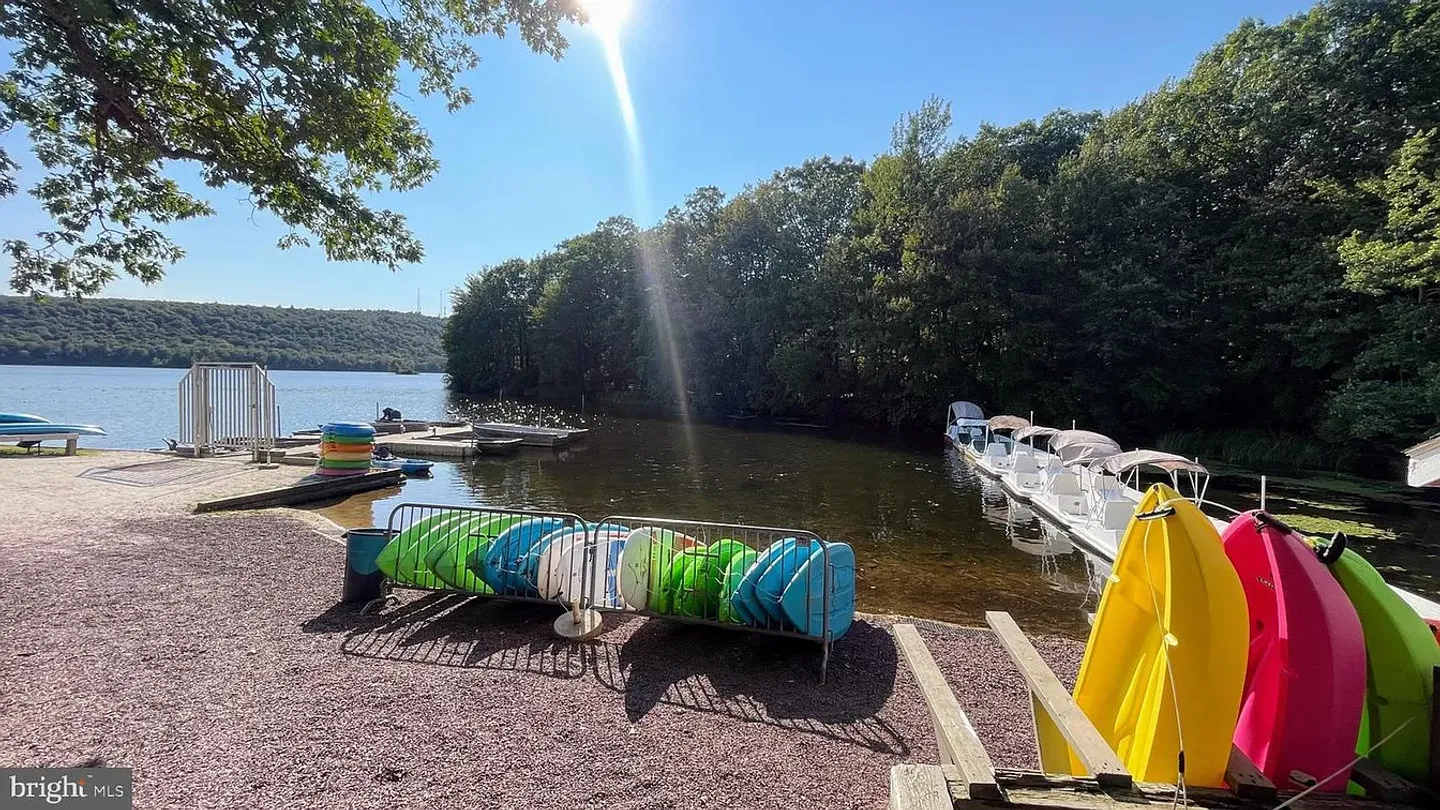 Lakeside boat launch area with racks of kayaks and pedal boats docked along the shore on a sunny day.