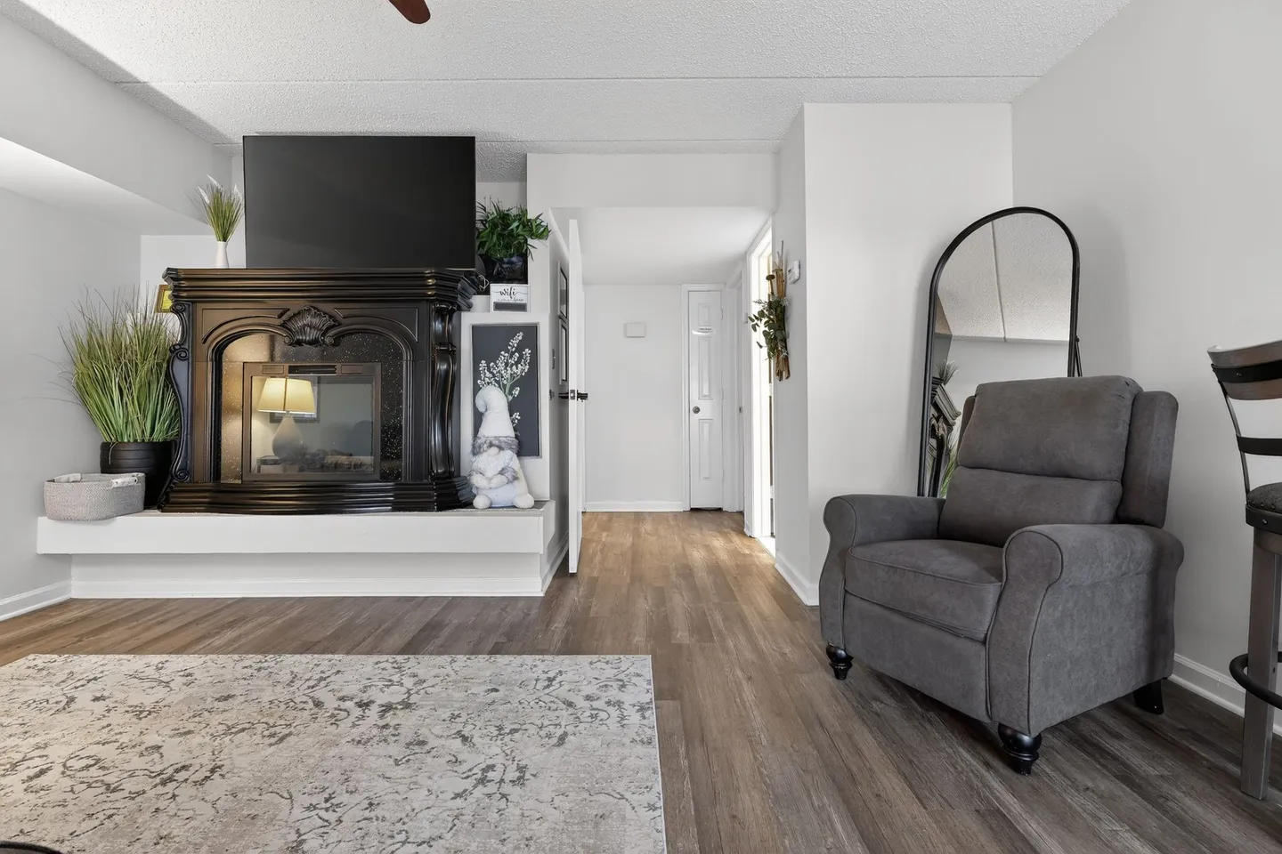 Living room area featuring wood-style flooring, a dark decorative fireplace, an armchair, and a hallway leading into other rooms.