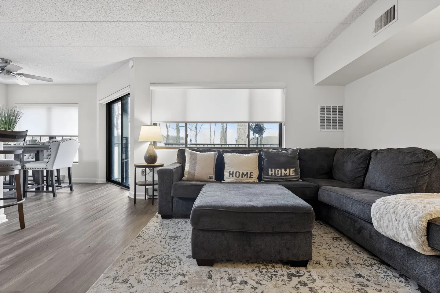 Living room featuring a dark gray sectional sofa with matching ottoman on an area rug, adjacent to a dining area.