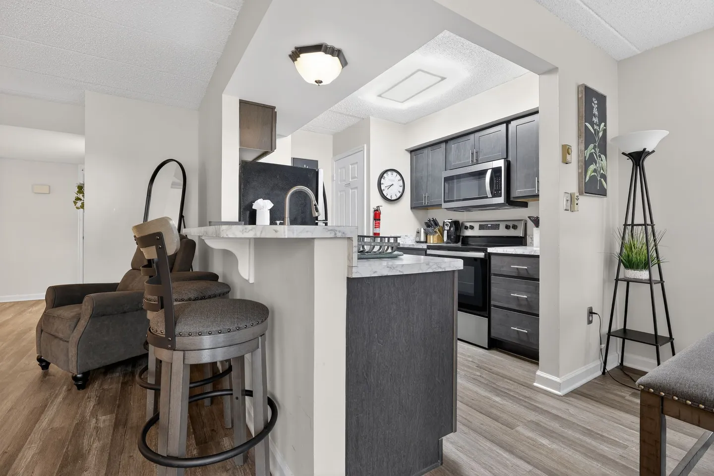 Kitchen with dark cabinetry and breakfast bar counter with barstool seating next to a living area.