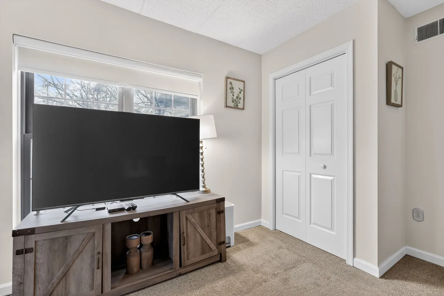 A flat-screen television positioned on a rustic wooden media console in a carpeted room next to a white closet door.
