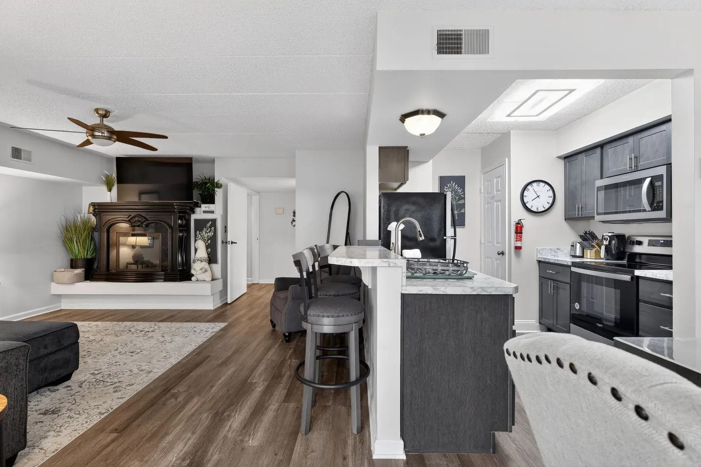 Open-concept living room and kitchen area featuring wood-look flooring, a kitchen counter with barstools, and a fireplace with a TV above it in the living room.