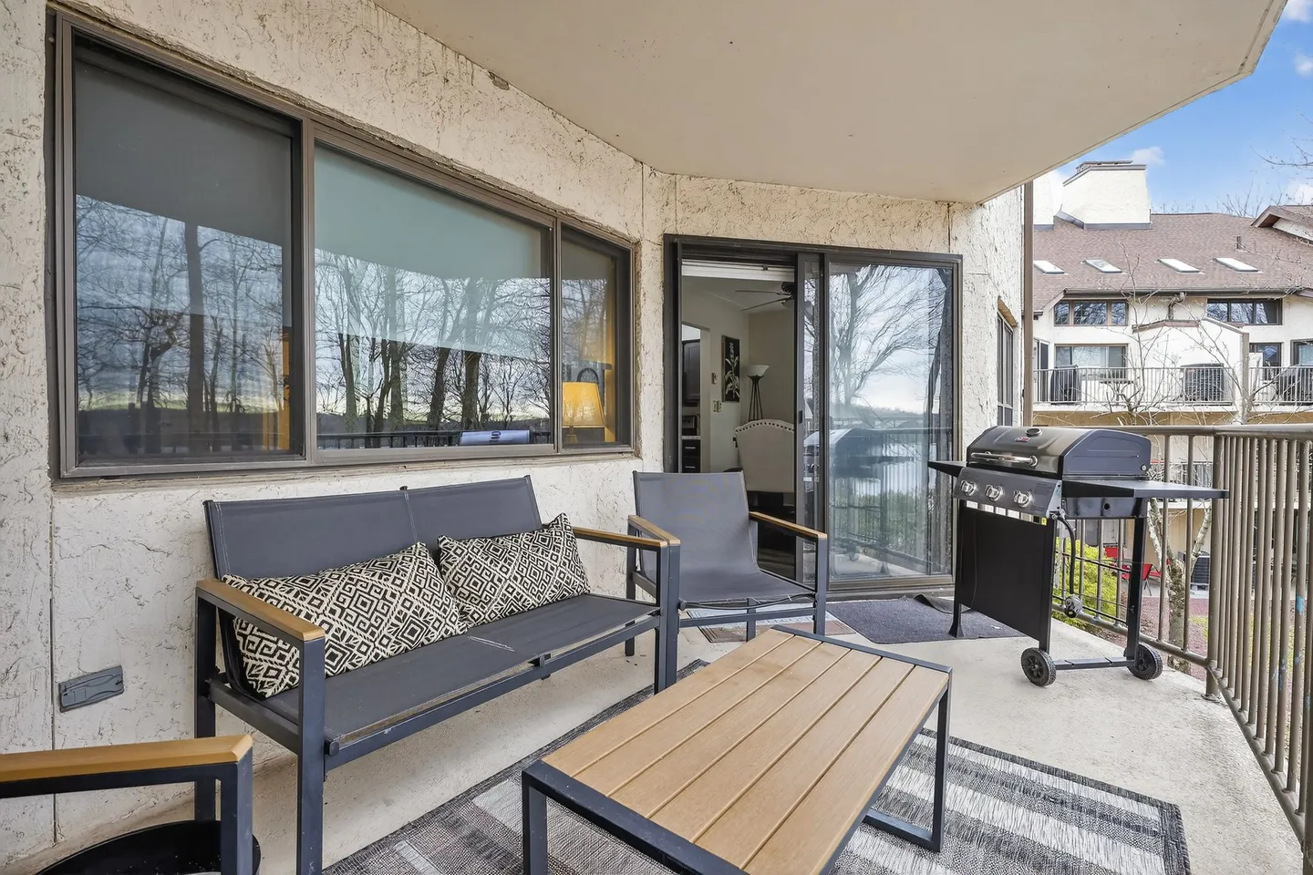 Balcony with outdoor seating, a coffee table, and a gas grill next to sliding glass doors.