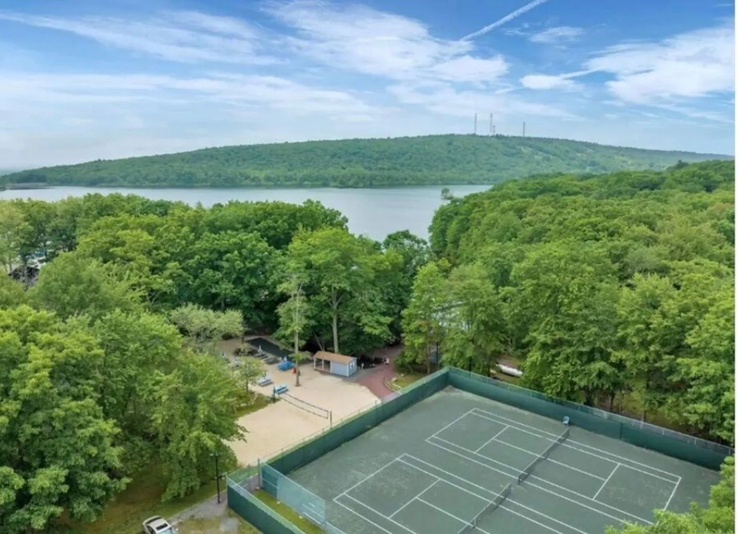 Aerial view of community amenities including tennis courts, a sand volleyball court, and a nearby lake surrounded by lush green trees.