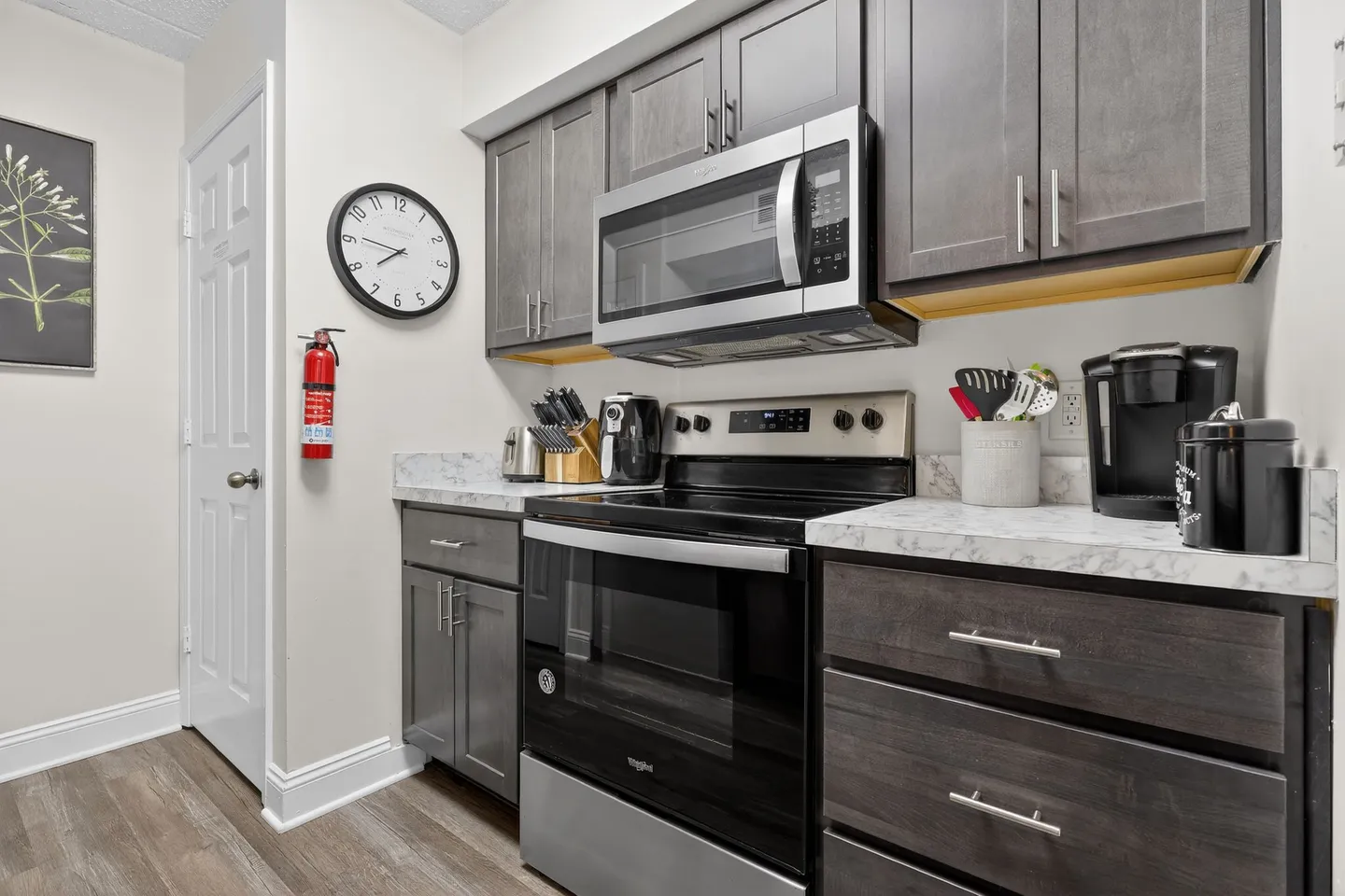 A kitchen with dark gray shaker-style cabinets, a stainless steel microwave mounted over an electric range, and light marble-patterned countertops.