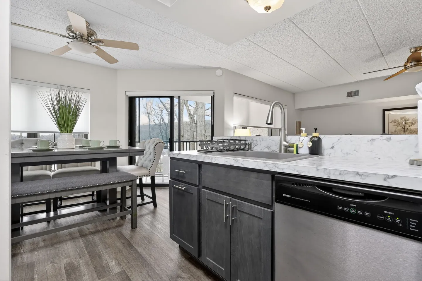 Kitchen counter with sink and dishwasher looking towards a dining area with table and sliding glass door leading to a balcony.
