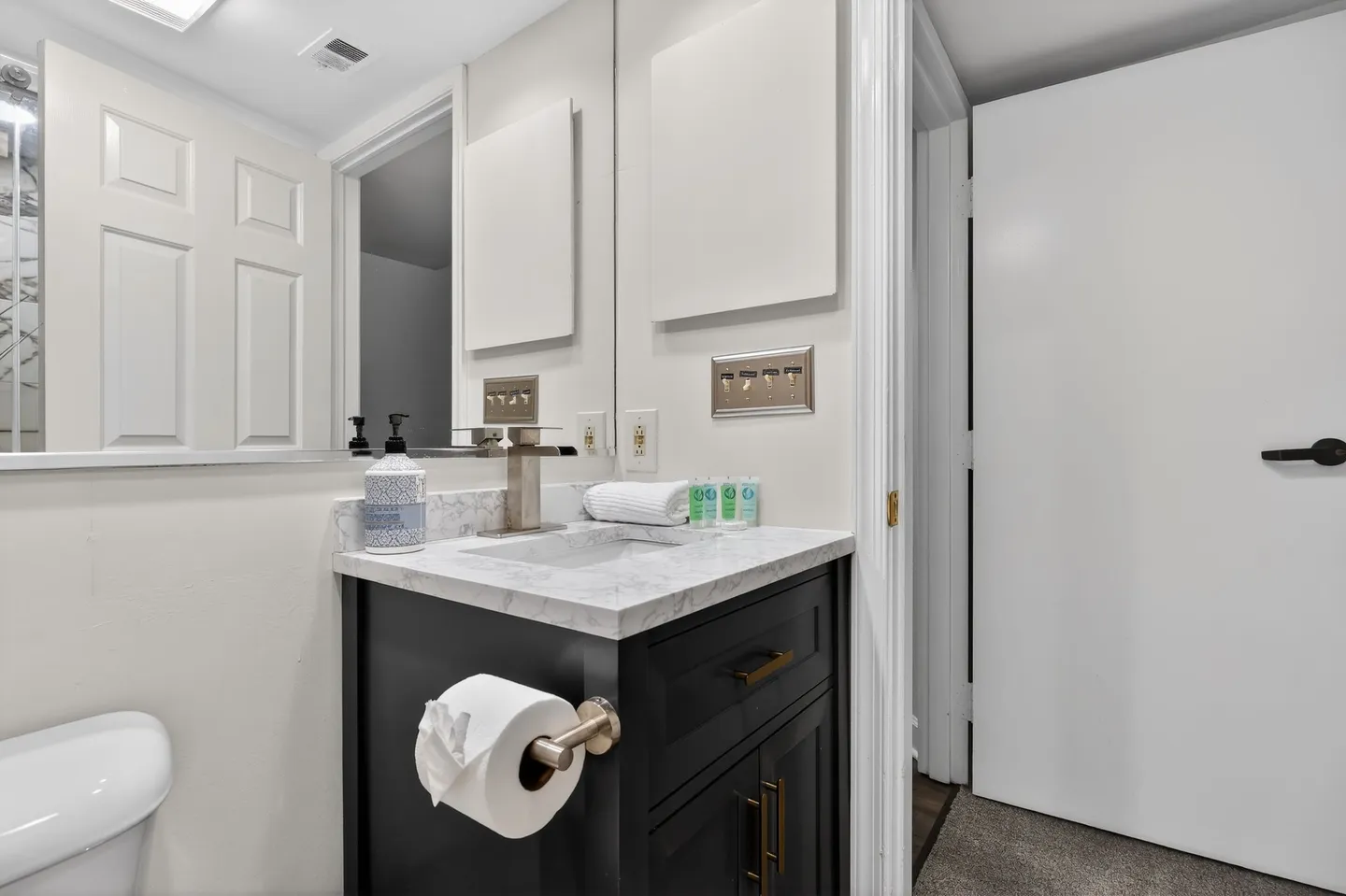 Bathroom vanity with a dark cabinet, marble-look countertop, rectangular undermount sink, modern faucet, mirror, and toilet roll holder.