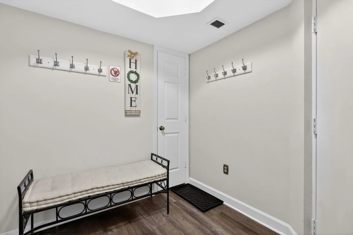 Entryway with a cushioned metal bench, coat hooks on light walls, and a white interior door.