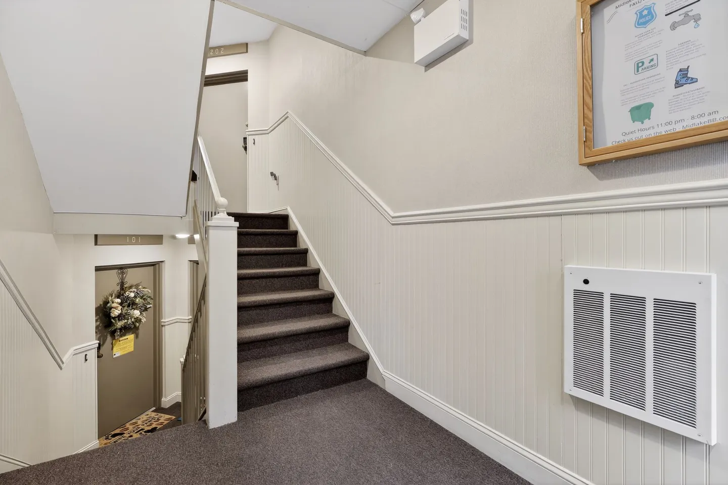 An interior carpeted staircase in a shared building hallway with wainscoting on the walls.