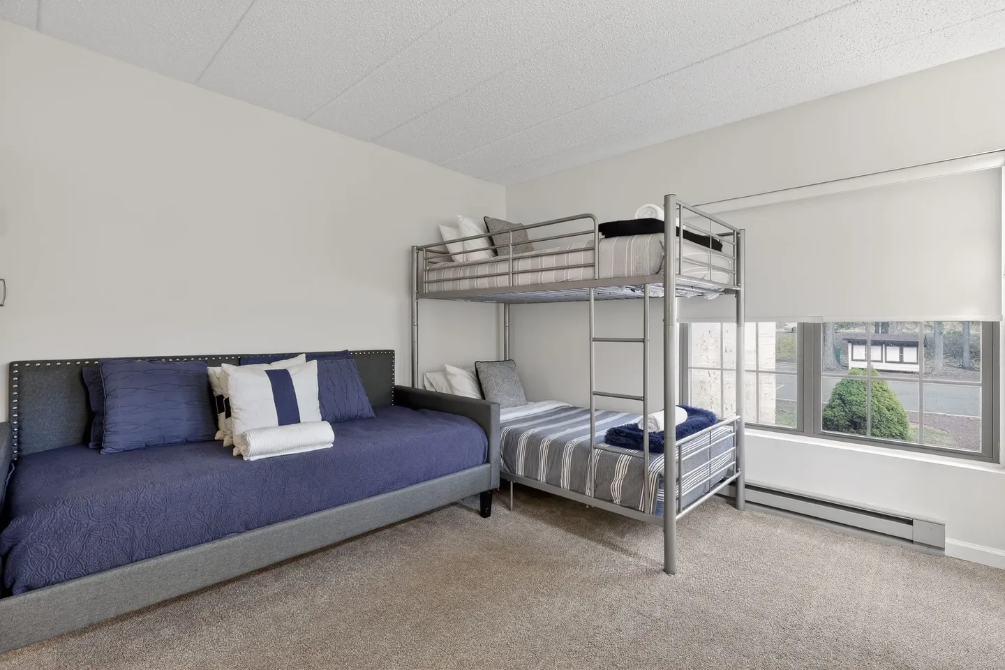 Bedroom featuring a daybed with blue bedding, a silver metal bunk bed, and a window overlooking greenery.