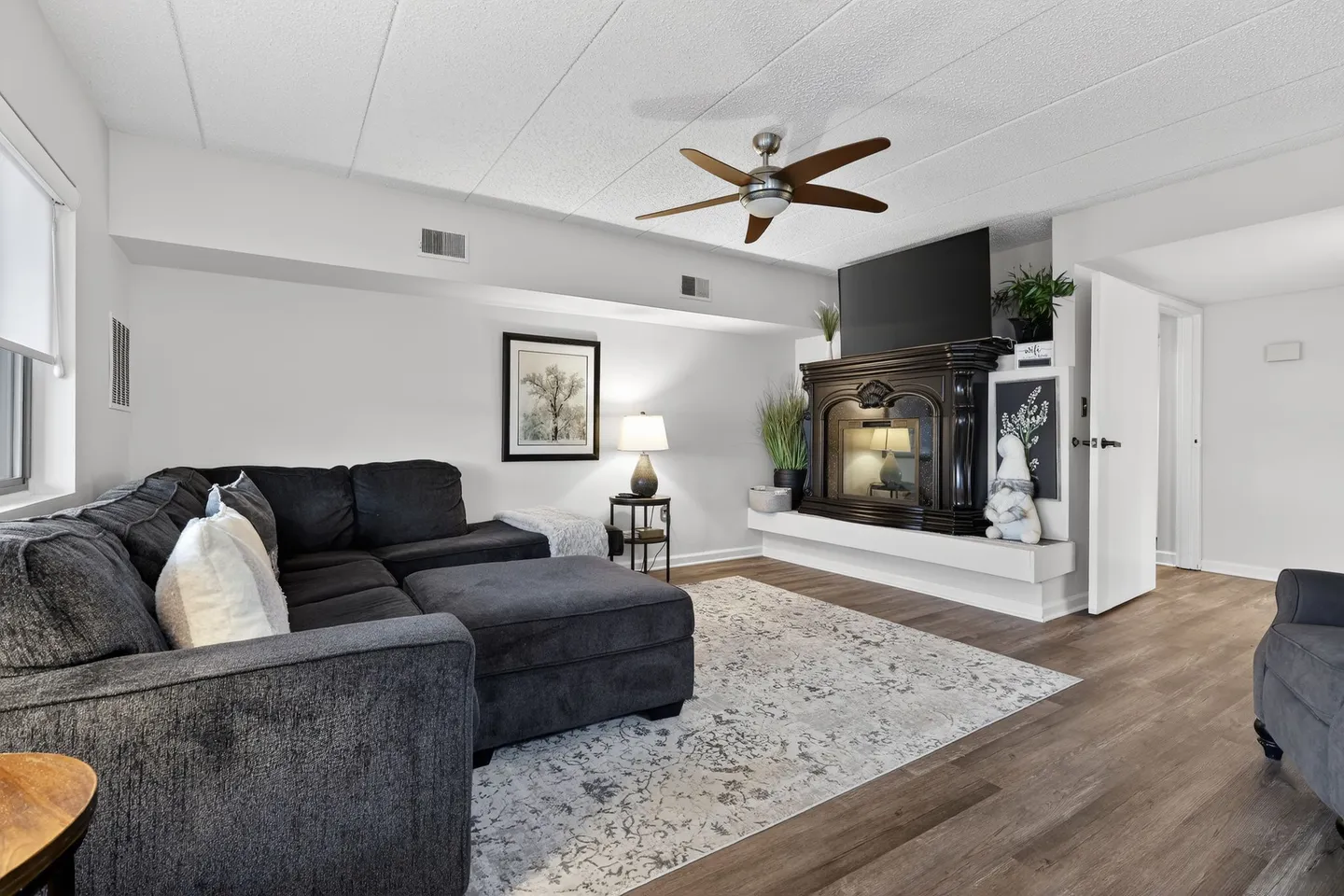 Living room featuring a dark gray sectional sofa, an area rug, a ceiling fan, and a fireplace with a mounted television above.