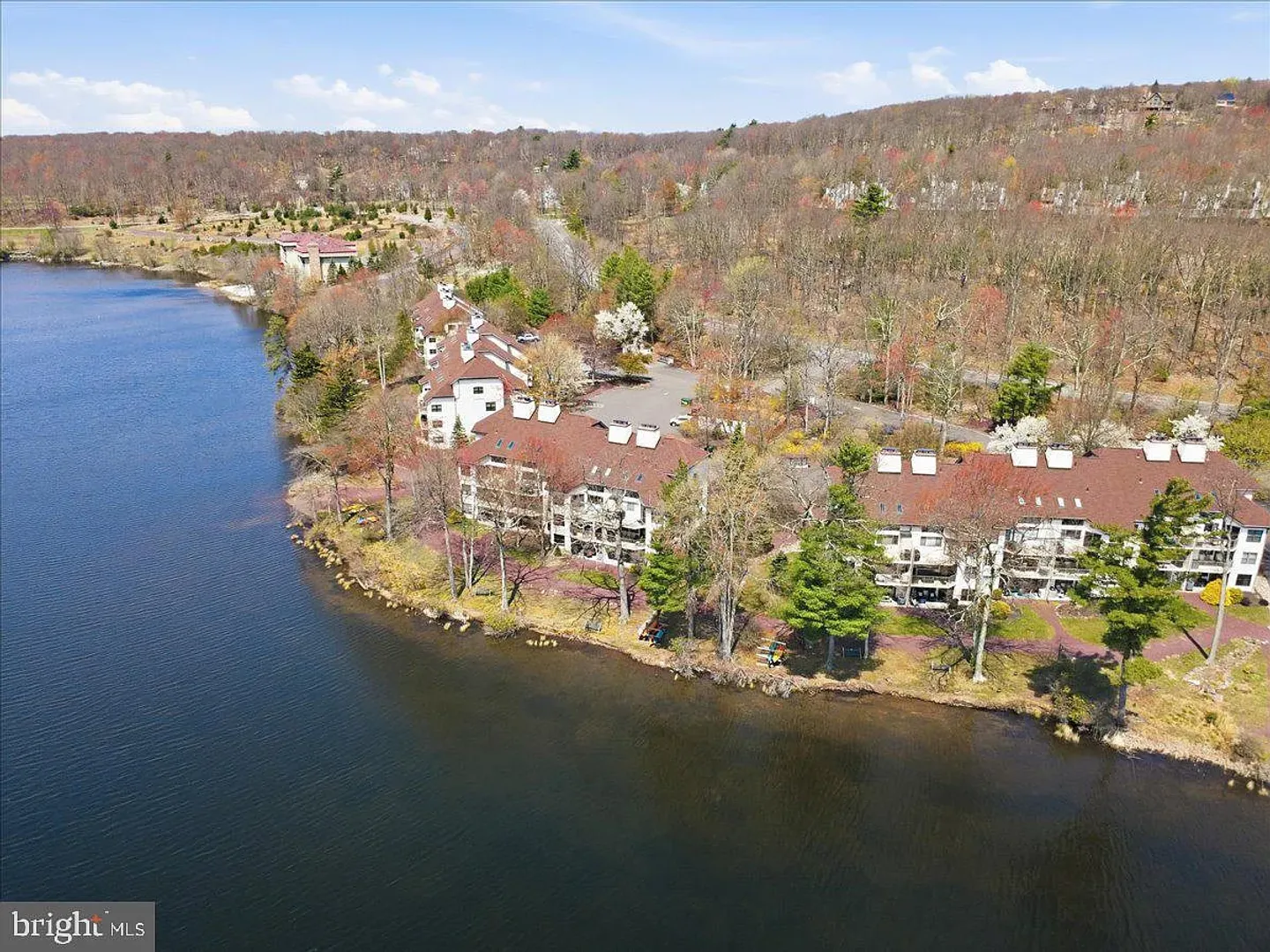 Aerial view of a lakefront condominium complex surrounded by trees with rolling hills in the background.