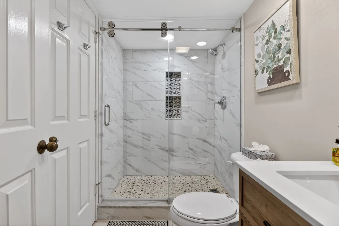 Bathroom showing a walk-in shower with sliding glass doors, white toilet, and corner of a vanity.