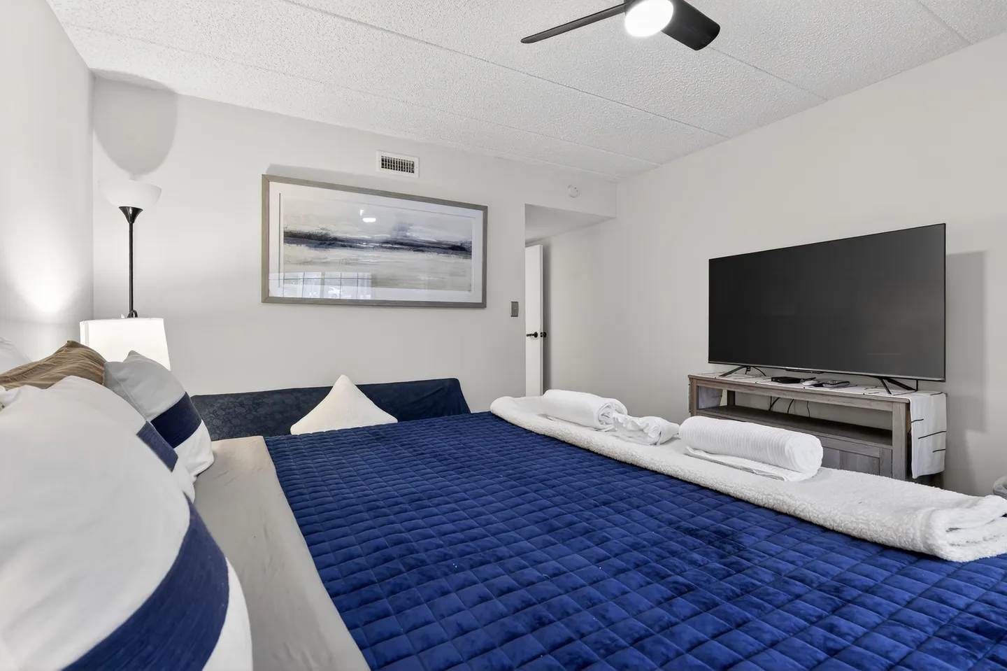 Bedroom featuring a bed with a royal blue textured bedspread facing a large flat-screen TV on a media console.