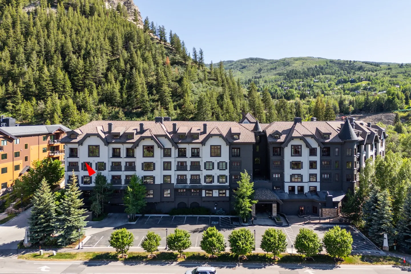 Aerial view of a multi-story lodge-style condominium building nestled against a pine-covered hillside.