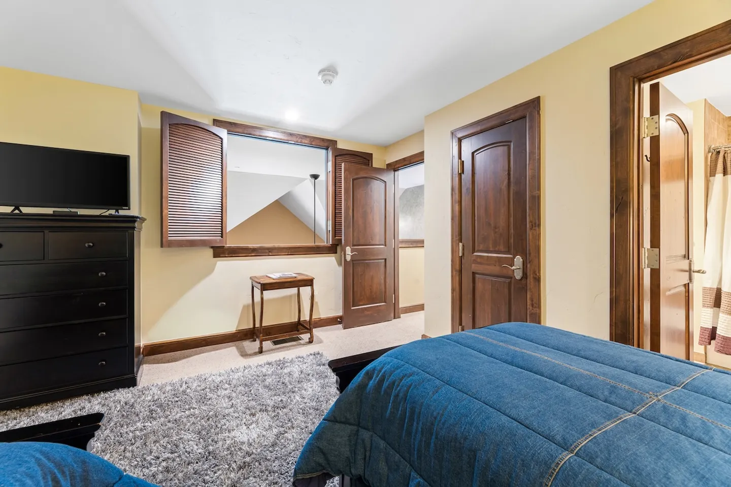 Bedroom with yellow walls, dark wood doors, a bed with a blue denim-style bedspread, and an interior window opening.