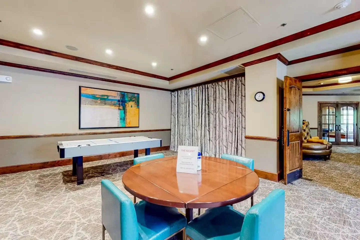 Game room featuring a round card table with blue chairs, an air hockey table, and patterned carpeting.