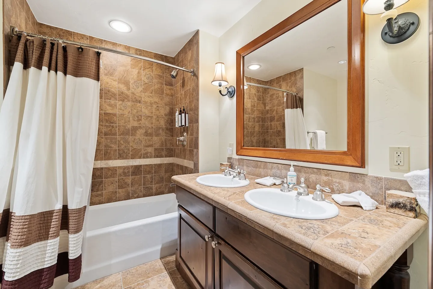 Bathroom with a double-sink vanity, tiled countertop, large mirror, and tiled shower/tub combo with a striped curtain.