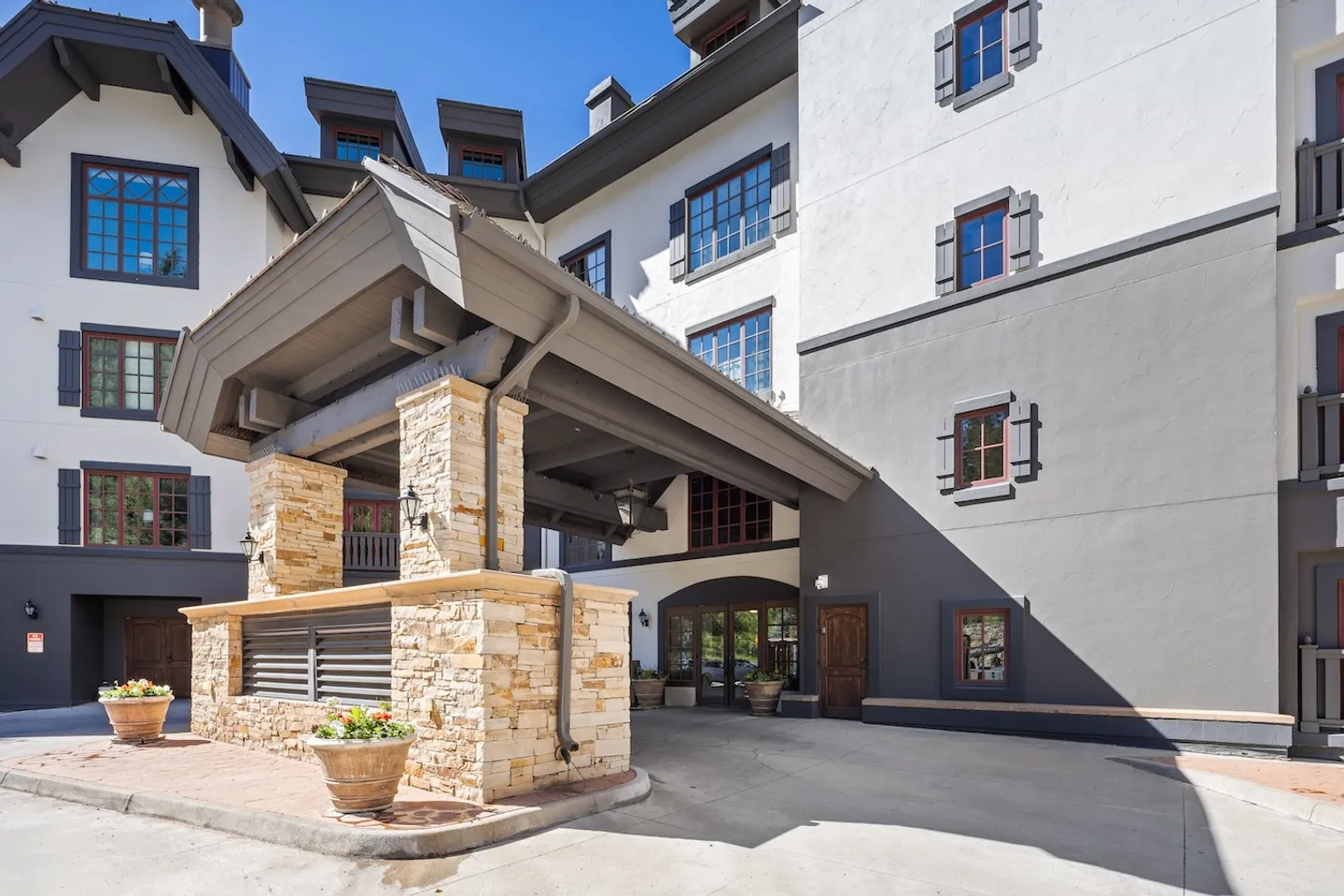 Covered drive-through entrance of a multi-story lodge-style building with stone pillars and timber canopy.